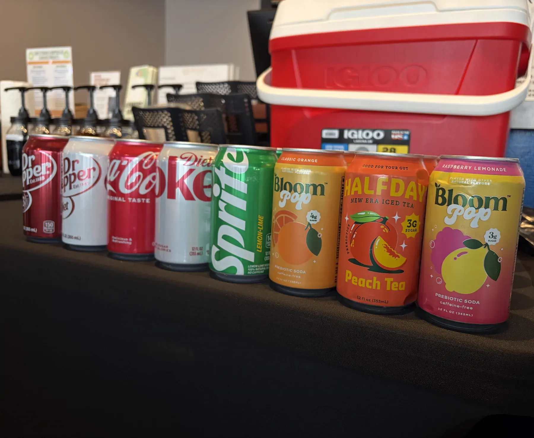 The Sip Well base lineup on a counter: Dr Pepper, Coke, Sprite, Bloom prebiotic soda and Halfday iced tea beside the syrup pumps